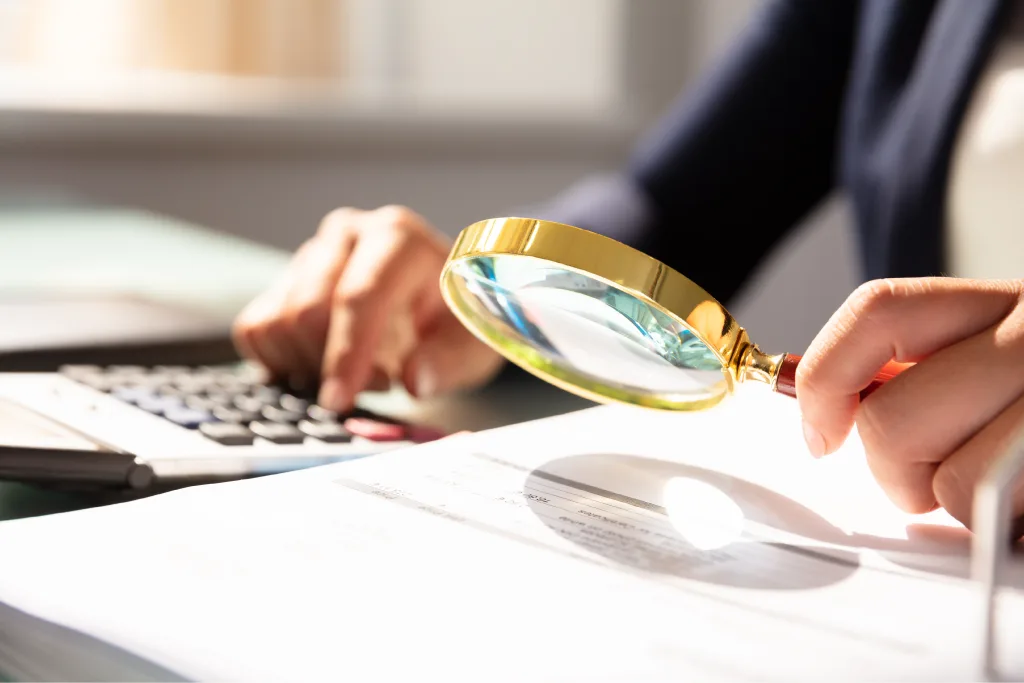Person using a magnifying glass to look closer at paperwork.