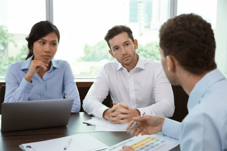 Woman and man in a meeting with another man discussing paperwork.