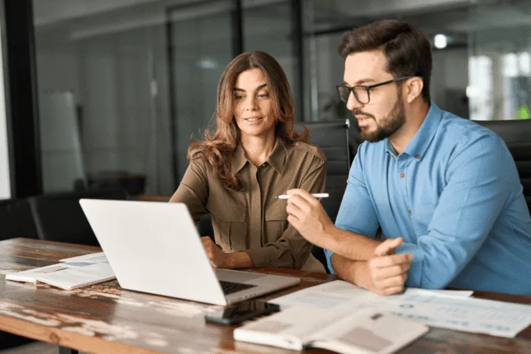 A woman and man sit beside each other looking at a laptop as they review open enrollment options and benefits information.